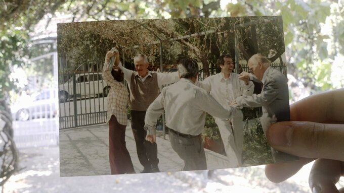 A hand holds up a photo against an outdoor backdrop. The photo features people dancing merrily.