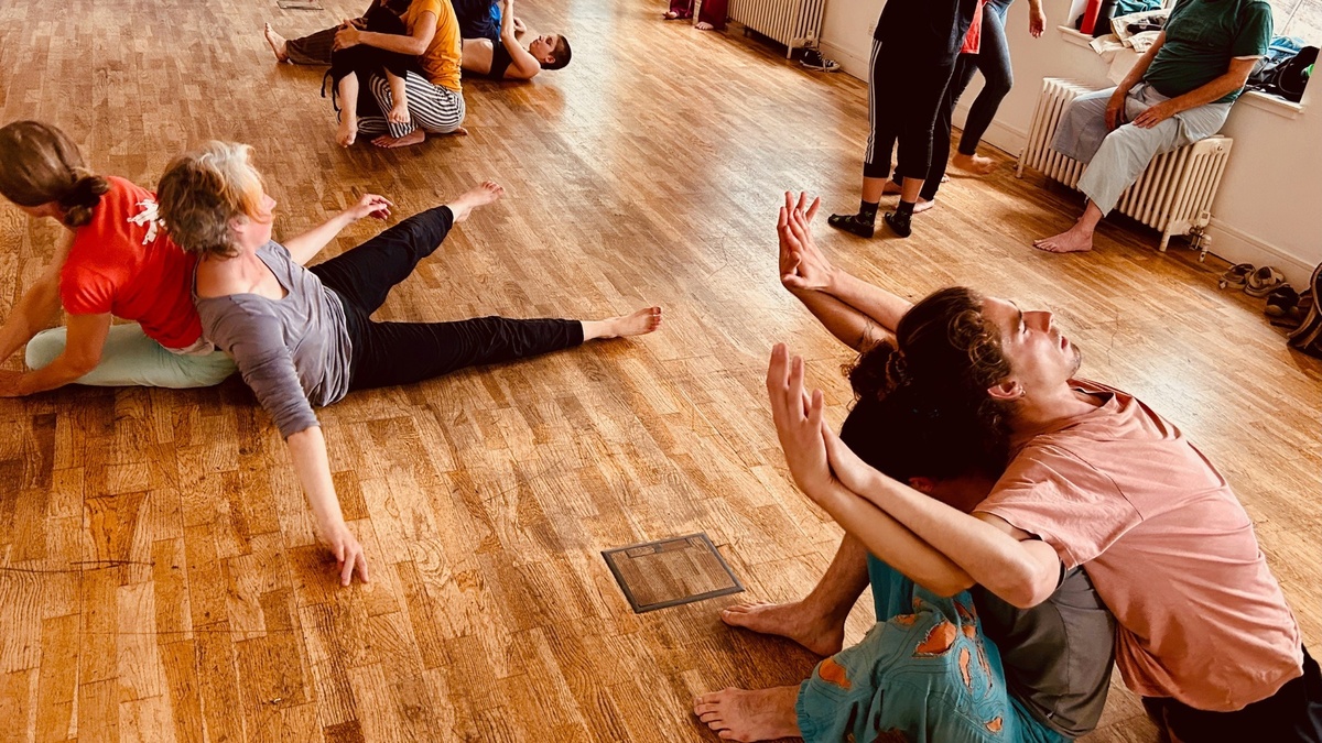 Dancers sitting on a wooden floor, waving arms in the air.