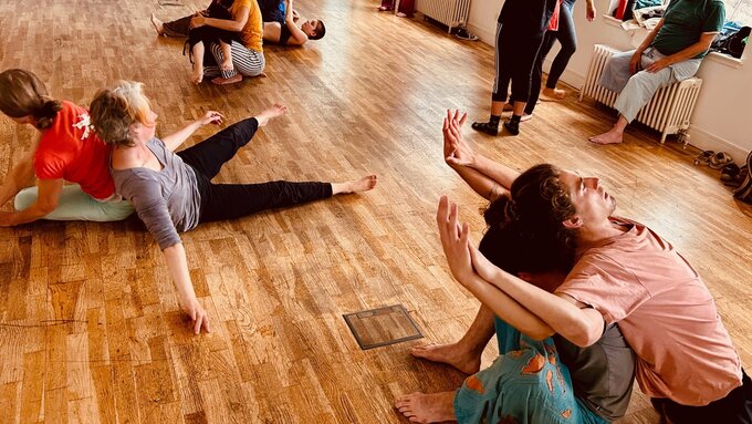 Dancers sitting on a wooden floor, waving arms in the air.