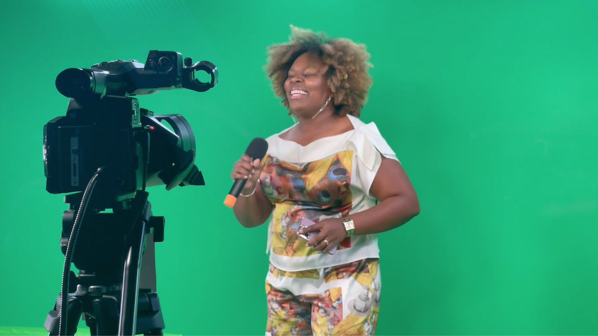 Captura image: A person with a microphone is smiling to a camera, set against a green screen.