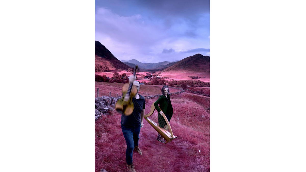 Two people stood among rolling hills with a violin and harp. The image is edited so the grass is purple.