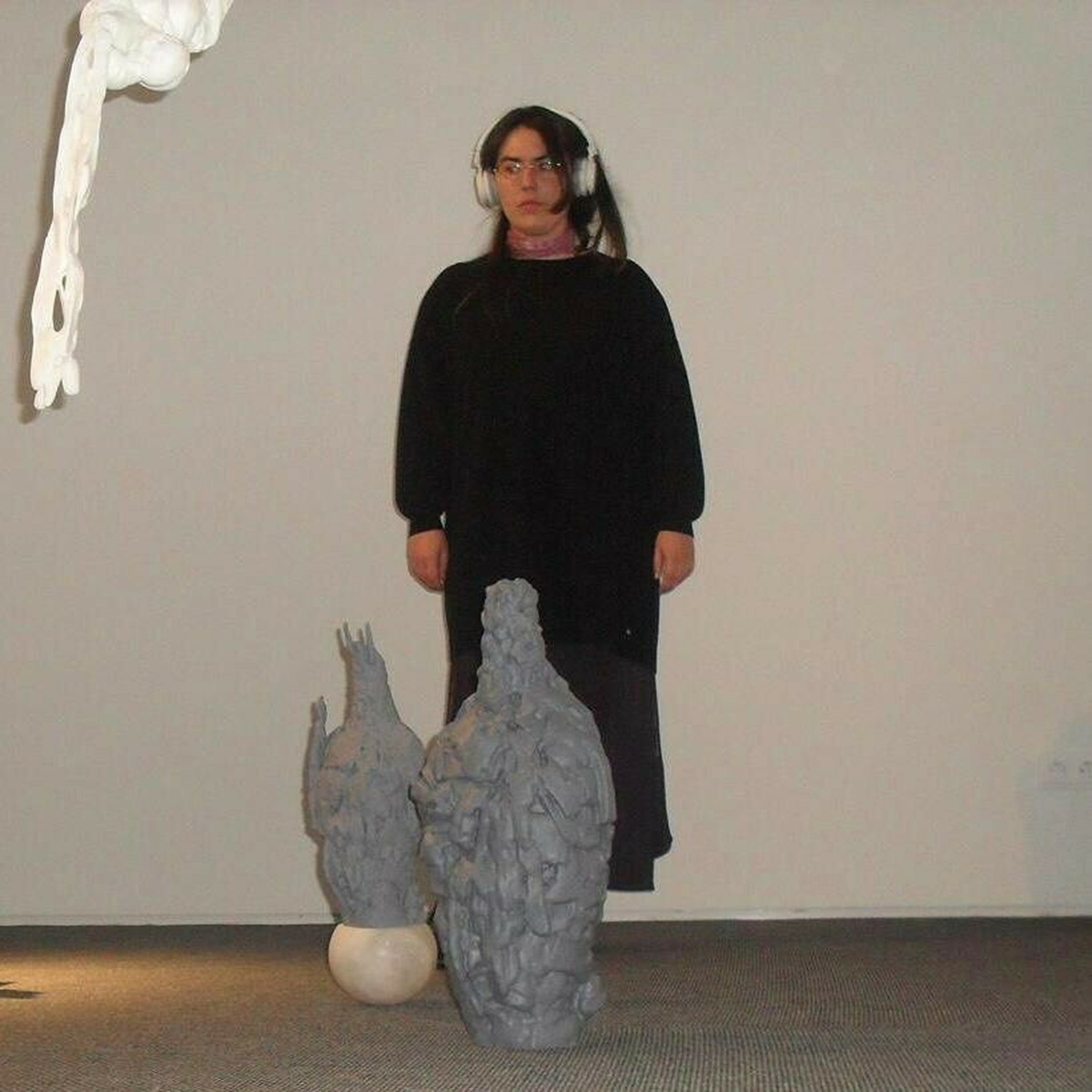 A woman wearing all black with white headphones stood behind too clay sculptures.