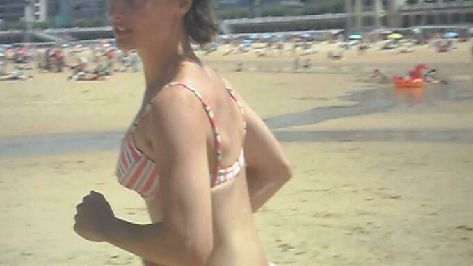 A grainy video still: A woman wearing a bikini running across a busy beach on a sunny day.