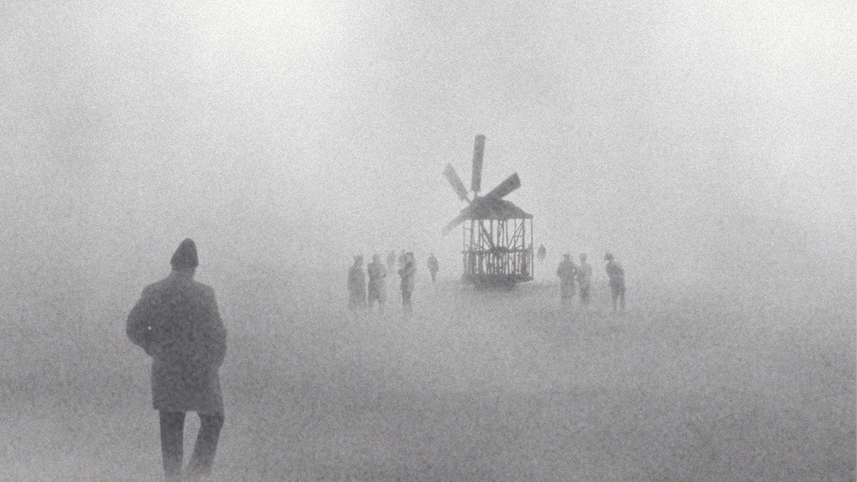 A figure looks on a distant windmill in a foggy landscape.