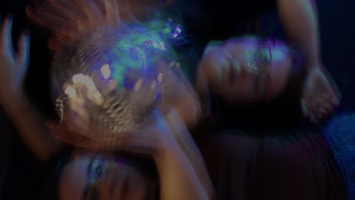 A blurred close-up shot of two people lying on the ground, interacting with a disco ball.