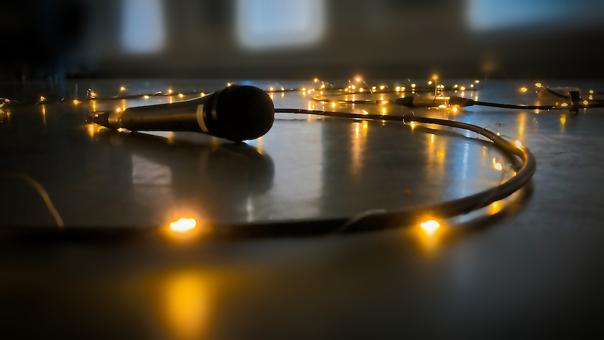 Fairy lights wrapped around a mic chord creating an illuminated scribble on the ground, with a microphone at the end.