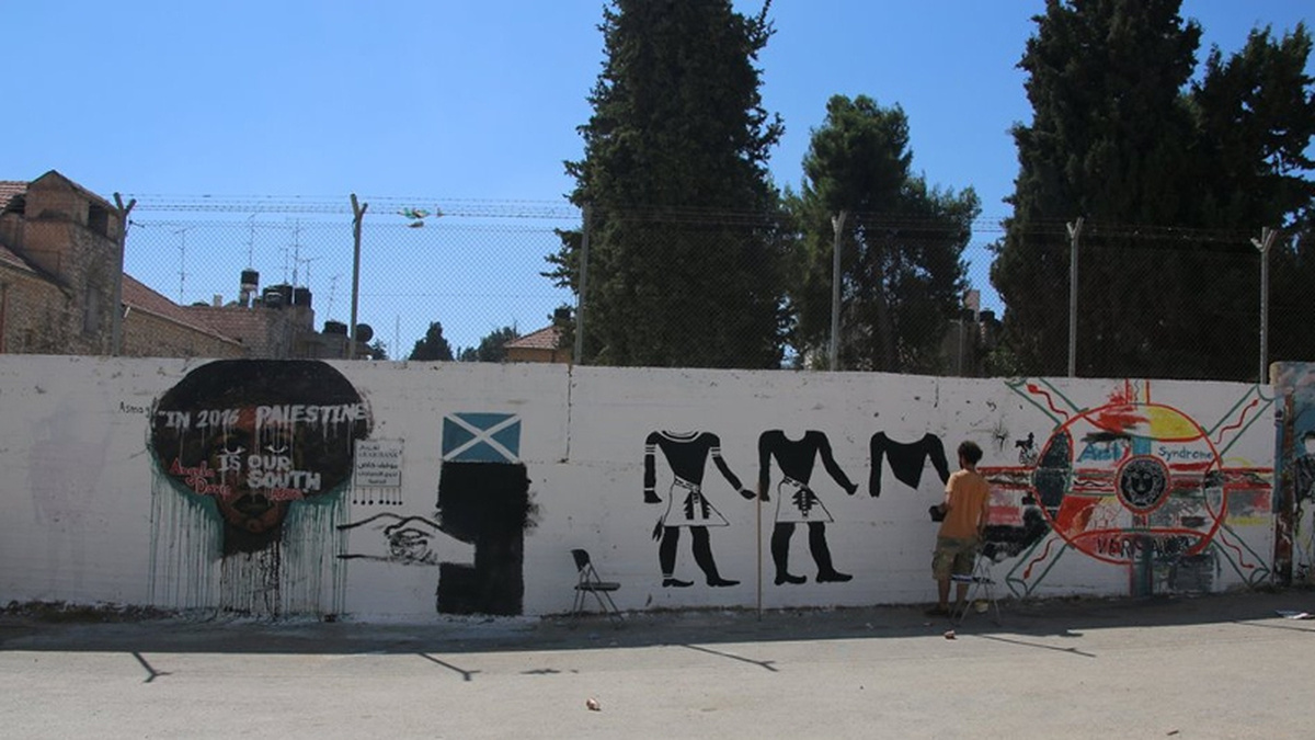 A wall in Palestine being painted with various symbols, such as a Scottish flag and hands grasping together.